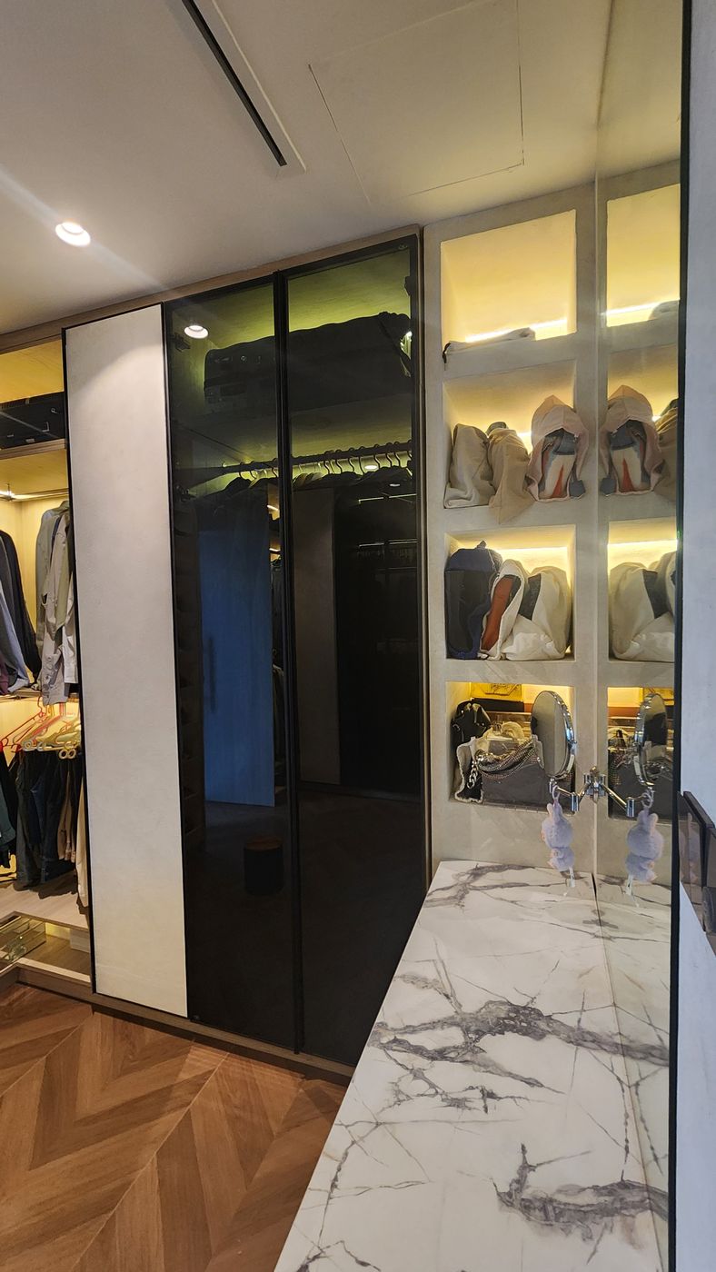 Dressing area with lit open shelves of bags, smoked-glass wardrobe doors and a marble-look counter