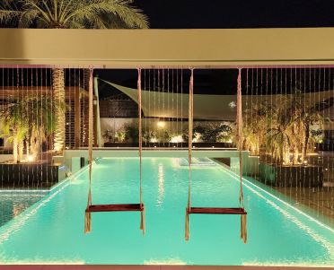 Swings hanging over the lit pool beneath a rain-shower frame at night, Project Casa Colonia, The Villa